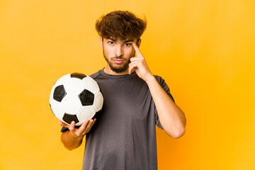Young soccer player indian man pointing temple with finger, thinking, focused on a task.
