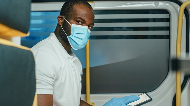 Black African American Paramedic in Face Mask Using Tablet Computer while Riding in Ambulance Vehicle for an Emergency. Emergency Medical Technicians Outside the Healthcare Hospital. Covid-19 Concept.