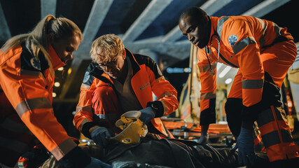 Fototapeta na wymiar Team of EMS Paramedics Provide Help to an Injured Young Man. Doctor in Gloves Attaches Cervical Neck Collar on a Patient. Emergency Care Assistants Arrived in an Ambulance Vehicle at Night.