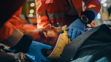 Team of EMS Paramedics Provide Help to an Injured Young Man. Doctor in Gloves Attaches Cervical...