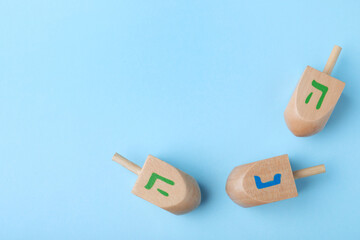 Hanukkah traditional dreidels with letters He and Nun on light blue background, flat lay. Space for text