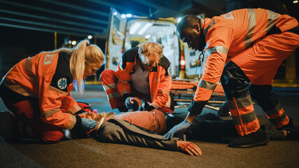Team of EMS Paramedics Bring a Stretcher from Ambulance Vehicle and Help an Injured Young Person. Emergency Care Assistants Arrived on the Scene of a Traffic Accident on a Street at Night. - obrazy, fototapety, plakaty