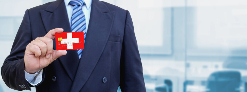 Cropped image of businessman holding plastic credit card with printed flag of Switzerland. Background blurred.