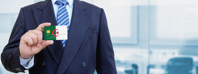 Cropped image of businessman holding plastic credit card with printed flag of Algerian. Background...