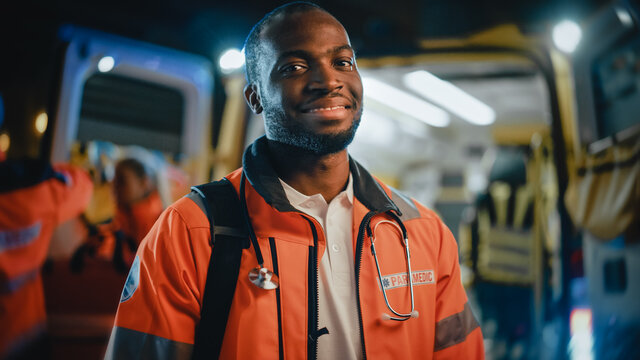 Portrait of a Black African American EMS Paramedic Proudly Standing in Front of Camera in High Visibility Medical Orange Uniform and Smiling. Successful Emergency Medical Technician or Doctor at Work.