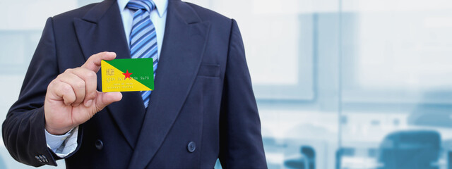 Cropped image of businessman holding plastic credit card with printed flag of French Guiana. Background blurred.