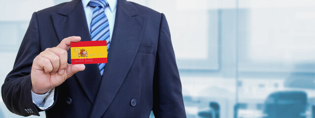 Cropped image of businessman holding plastic credit card with printed flag of Spain. Background...