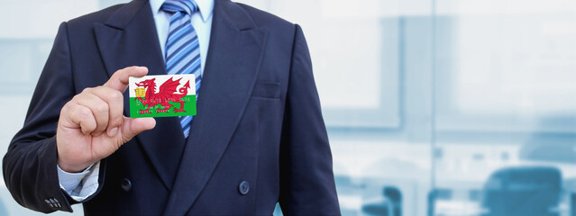Cropped image of businessman holding plastic credit card with printed flag of Wales. Background...