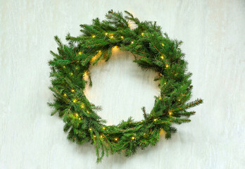 Beautiful Christmas wreath with festive lights on white wooden background, top view