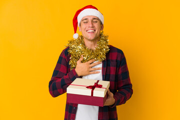 Young caucasian man with christmas hat holding a present isolated on yellow background