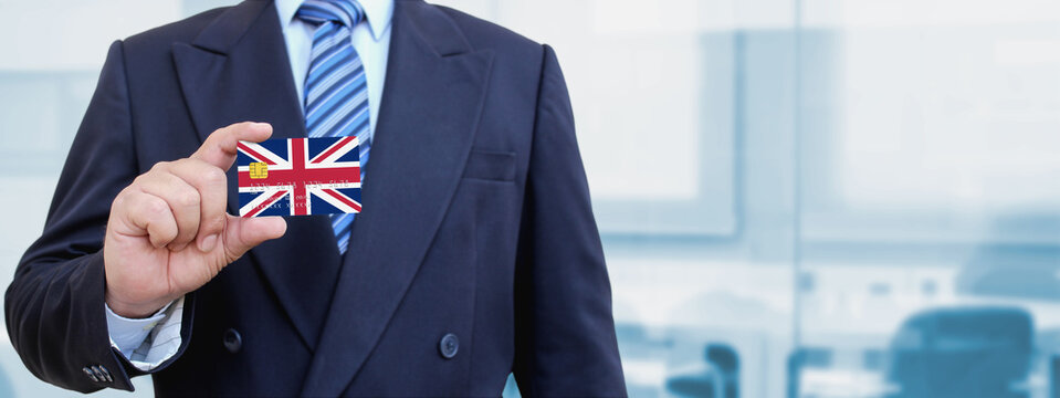 Cropped image of businessman holding plastic credit card with printed flag of United Kingdom. Background blurred.