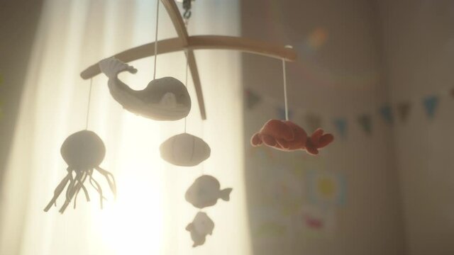 Rotating Wooden Crib Toy with Stuffed Animals Hanging Above Newborn Baby Bed. Cozy, Sunny and Authentic Kids Bedroom with Colorful Drawings on Walls. Concept of Childhood, New Llife and Parenthood.
