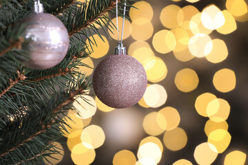 Shiny pink balls hanging on Christmas tree against festive lights, closeup