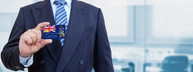 Cropped image of businessman holding plastic credit card with printed flag of South Georgia and the South Sandwich Islands. Background blurred.