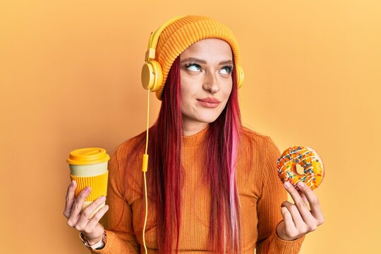 Young caucasian woman having breakfast using headphones smiling looking to the side and staring away thinking.