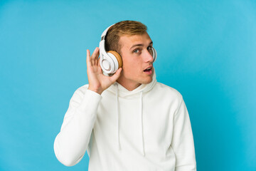 Young caucasian man listening music isolated on blue background