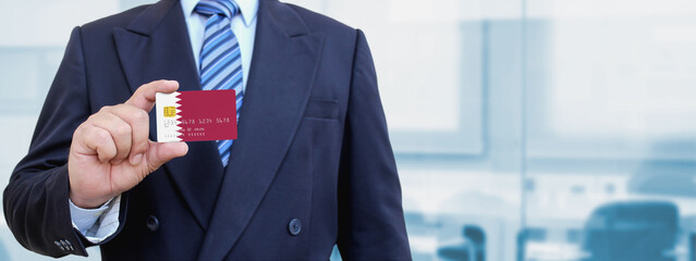 Cropped image of businessman holding plastic credit card with printed flag of Qatar. Background blurred.