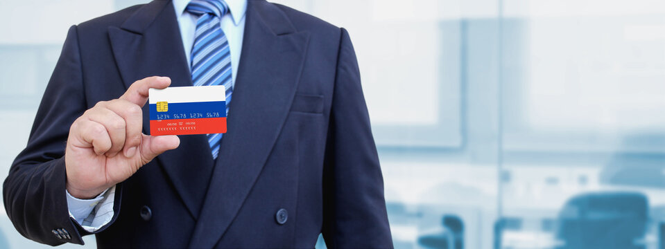 Cropped image of businessman holding plastic credit card with printed flag of Russia. Background blurred.