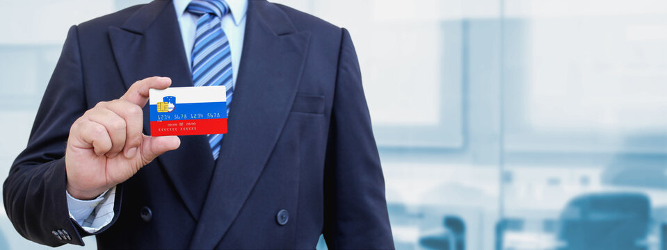Cropped image of businessman holding plastic credit card with printed flag of Slovenia. Background blurred.