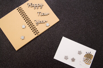 wooden letters, christmas tree lie on an open notebook. two white postcards on a black background.
