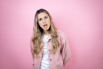 Young beautiful blonde woman with long hair standing over pink background afraid and shocked with surprise and amazed expression, fear and excited face.