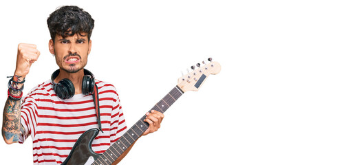 Young hispanic man playing electric guitar annoyed and frustrated shouting with anger, yelling crazy with anger and hand raised