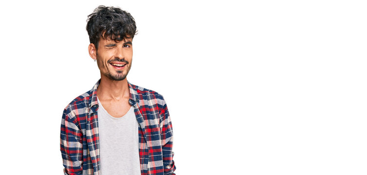 Young hispanic man wearing casual clothes winking looking at the camera with sexy expression, cheerful and happy face.