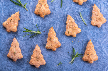 Homemade Christmas tree shaped cookies baked from whole grain spelt wheat and cheese, flavoured with rosemary on blue stone surface