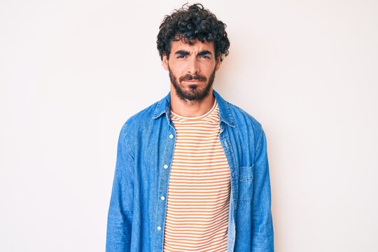 Handsome young man with curly hair and bear wearing casual denim jacket skeptic and nervous, frowning upset because of problem. negative person.