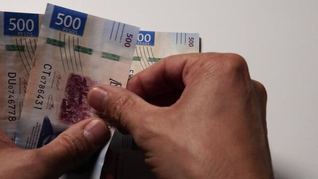 Unas manos cuentan billetes de 500 y de 200 pesos mexicanos frente a la c&aacute;mara sobre una mesa blanca