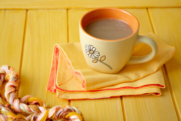 Cappuccino with coffee art in orange cup on yellow wooden table.
