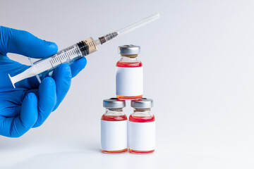 medical person holding syringe near vials with red liquid over gray background. blank label on vials. copy space. vaccination concept