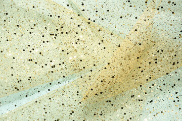 Sheer fabric layers with gold glitter on light blue background.