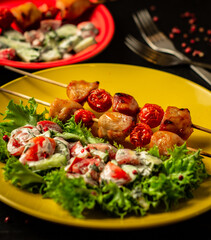 Chicken shashlyk with tomatoes on a wooden skewer with salad. Tasty homemade baked meat served with summer vegetables in yellow plate
