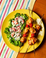 Chicken shashlyk with tomatoes on a wooden skewer with salad. Tasty homemade baked meat served with summer vegetables in yellow plate