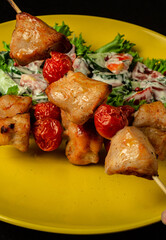 Chicken shashlyk with tomatoes on a wooden skewer with salad. Tasty homemade baked meat served with summer vegetables in yellow plate