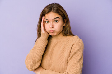 Young skinny caucasian girl teenager on purple background blows cheeks, has tired expression. Facial expression concept.