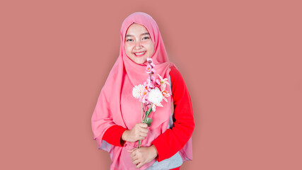 Portrait of a cute happy asian hijab woman holding flowers over red background. Looking at camera