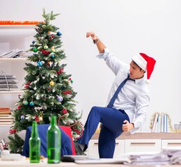 Young handsome employee celebrating Christmas at workplace