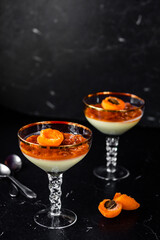 Tasty italian dessert panna cotta with apricot jam layer with green plant background. Low key. Vertical orientation. Negative space.