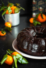 Pumpkin bundt cake with chocolate ganache and chocolate drops on a dark table. New year style and tangerines background. Vertical orientation.