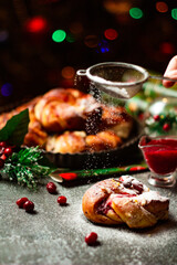 Fototapeta na wymiar Tasty homemade braided bun with cranberry jam and sugar powder. Christmas and New Year decorations. Bokeh lights background. Vertical orientation