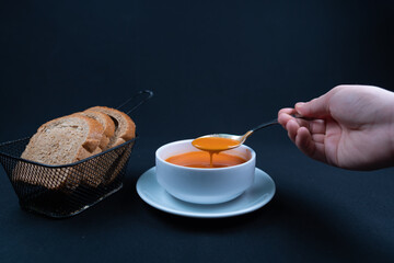 Tomato soup with basil, and bread in a bowl. Dark background.
