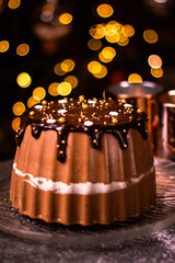 Tasty Three Chocolates mousse cake with ganache in Christmas and New Year decorations. Chocolate cake with layers. Bokeh lights background. Vertical orientation. Christmas Eve. Low Key.