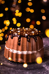 Tasty Three Chocolates mousse cake with ganache in Christmas and New Year decorations. Chocolate cake with layers. Bokeh lights background. Vertical orientation. Christmas Eve. Low Key.