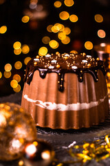 Tasty Three Chocolates mousse cake with ganache in Christmas and New Year decorations. Chocolate cake with layers. Bokeh lights background. Vertical orientation. Christmas Eve. Low Key.