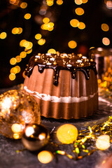 Tasty Three Chocolates mousse cake with ganache in Christmas and New Year decorations. Chocolate cake with layers. Bokeh lights background. Vertical orientation. Christmas Eve. Low Key.