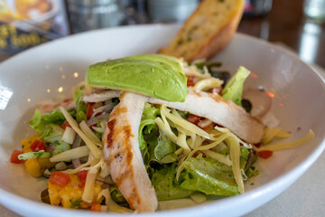 Chicken avocado salad with tomato salsa, slice of garlic bread in the back, soft focus