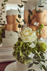 Wedding cake with white icing and copper gold color, with floral decorations and reflection in glass advertising of wedding planners, hotels or restaurants that are dedicated to organizing events.