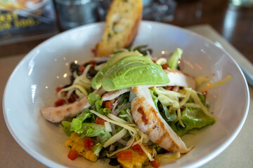 Chicken avocado salad with tomato salsa, slice of garlic bread in the back, soft focus